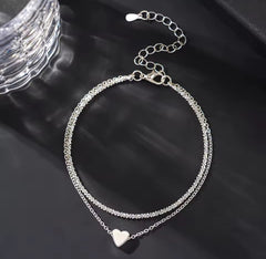 This is a minimalist, silver-plated double-layer ankle bracelet featuring a delicate heart charm and a shimmering chain.
