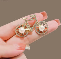 a gold-colored alloy bicycle brooch with faux pearl and rhinestone accents