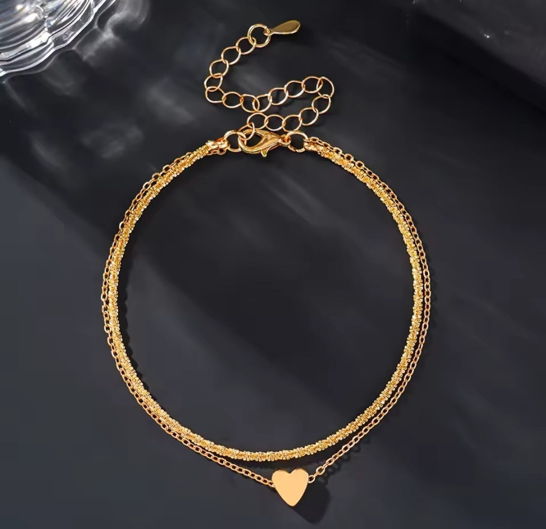 This is a minimalist, gold-plated double-layer ankle bracelet featuring a delicate heart charm and a shimmering chain.