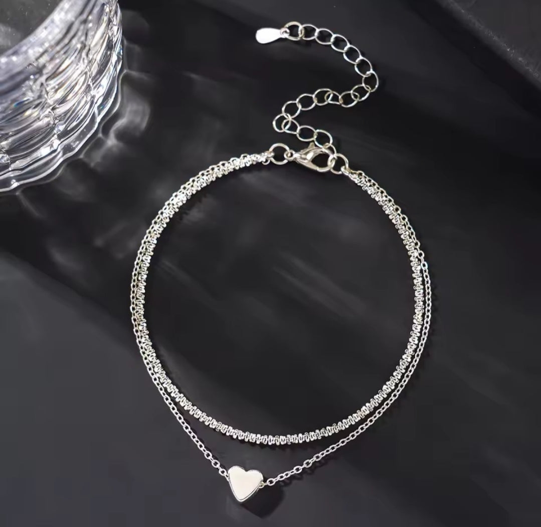 This is a minimalist, silver-plated double-layer ankle bracelet featuring a delicate heart charm and a shimmering chain.