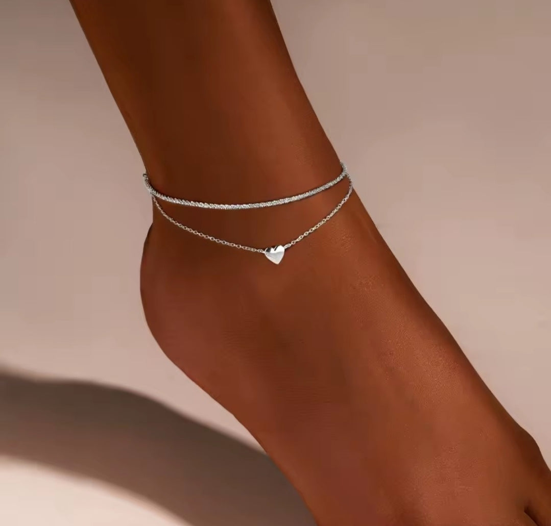 This is a minimalist, gold-plated double-layer ankle bracelet featuring a delicate heart charm and a shimmering chain.