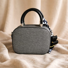 small grey structured handbag with a black top handle and a black and white gingham scarf detail, possibly from the brand Christian Dior